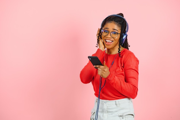 Portrait of a relaxed afro american woman in headphones listening music and using mobile phone isolated over pink background