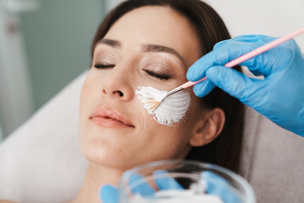 Portrait of relaxed caucasian woman getting cosmetic procedure by specialist while lying in beauty salon