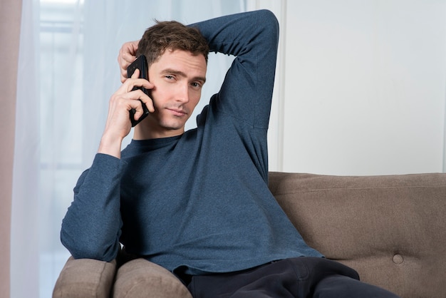 Portrait of relaxed handsome guy, young man is lying, sitting comfortable on a couch or sofa at home