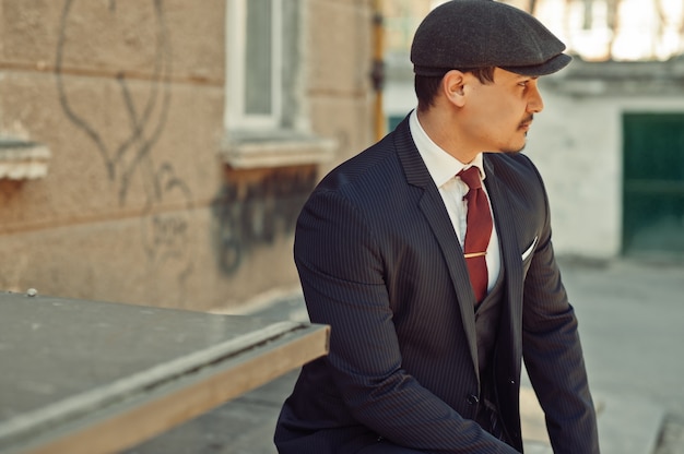 Portrait of retro 1920s english arabian business man wearing dark suit, tie and flat cap.