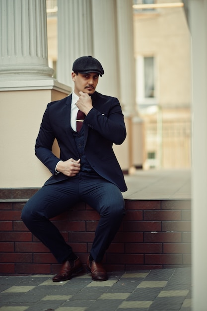 Portrait of retro 1920s english arabian business man wearing dark suit, tie and flat cap.