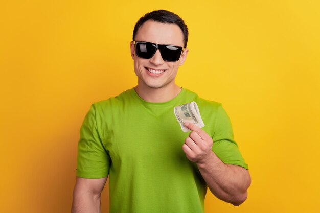 Portrait of rich millionaire guy hold dollar banknote smile wear sunglass on yellow background