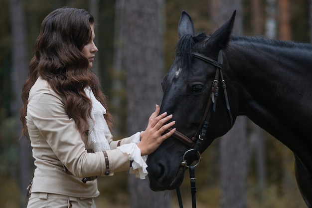 レトロなスーツを着たライダーと彼女の黒い馬の肖像画、若いブルネットが馬と接触する...