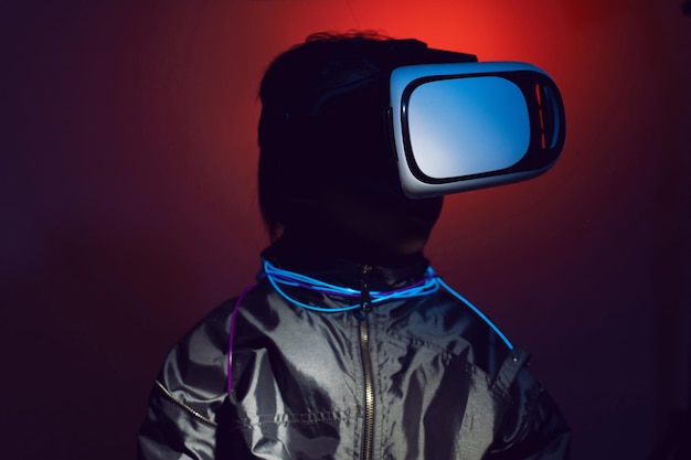 Portrait of robot boy child from the future in vr glasses and jacket looking at the phone at night