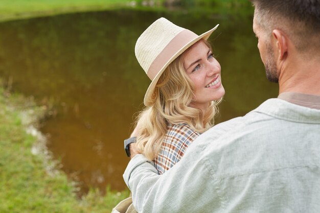 Portrait of romantic adult couple embracing while posing by lake in green countryside scenery