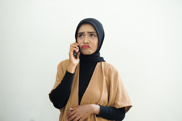 Portrait of a sad Asian Muslim woman wearing hijab making a call with a mobile phone