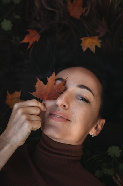 Portrait of sad beautiful young woman lying on the ground of an autumn forest with colorful maple leaves Concept blue monday