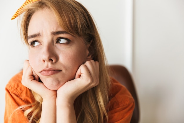 portrait of a sad displeased young blonde woman at home indoors posing sitting on chair.
