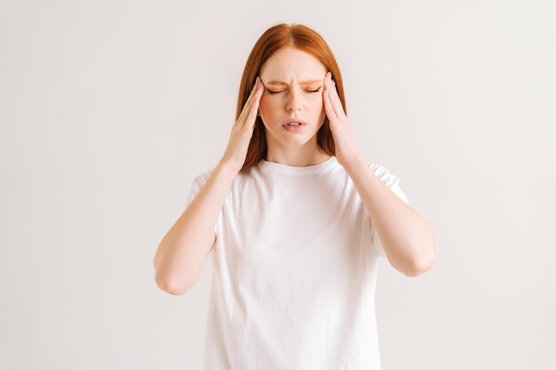 Portrait of sad exhausted young woman suffering from head ache and massaging temples by fingers