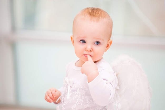 Portrait of a sad little girl angel with white wings weeping.