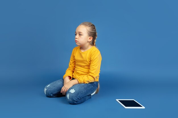 Portrait of sad little girl sitting isolated on blue studio\
background. how it feels to be autist. modern problems, new vision\
of social issues. concept of autism, childhood, healthcare,\
medicine.