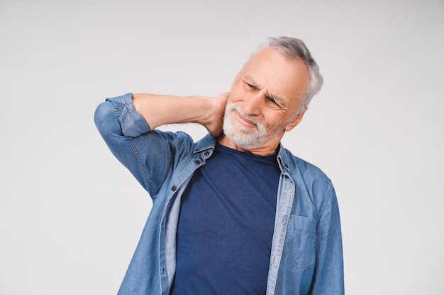 portrait of sad mature grayhaired man touching back of neck complaining on pain posing in studio