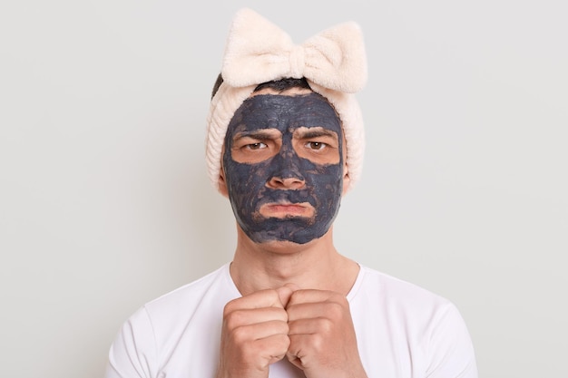 Portrait of sad offended handsome man with mud dirt cosmetology\
mask doing cosmetic procedures at home looking at camera with pout\
lips expressing sorrow