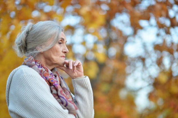 Портрет грустной пожилой женщины в осеннем парке