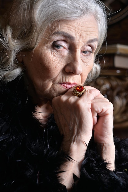 Portrait of sad senior woman in boa posing at home