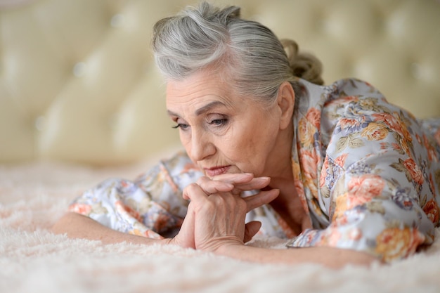 Portrait of sad senior woman lying on bed