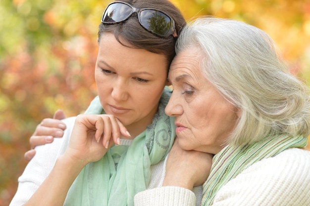 Portrait of sad senior woman with adult daughter in autumnal park