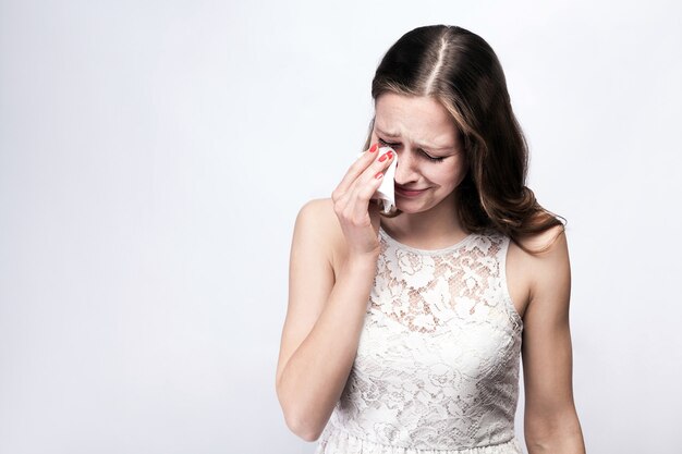 Portrait of sad, unhappy crying woman with freckles and white dress and smart watch on silver gray background. copy space. healthcare and medicine concept.