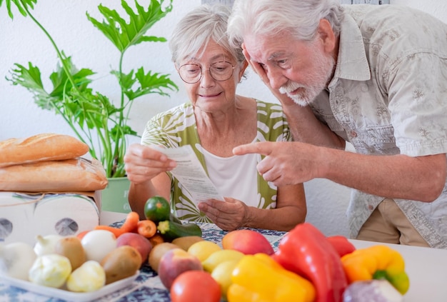 Portrait of sad unhappy worried old couple sitting at home table holding grocery receipt discussing for rising prices Bankruptcy financial difficulties concept Human emotions expressions