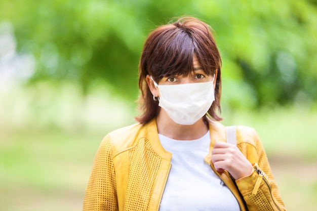 Portrait of sad unidentified woman posing in street in protective white medical mask on a sunny spring warm day. Concept of fatigue and sadness from coronovirus pandemic