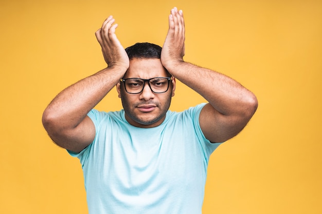 Portrait of sad updet or bored african american black indian young man standing and looking at camera with dissatisfied sadness face. Indoor studio shot, isolated on yellow background.