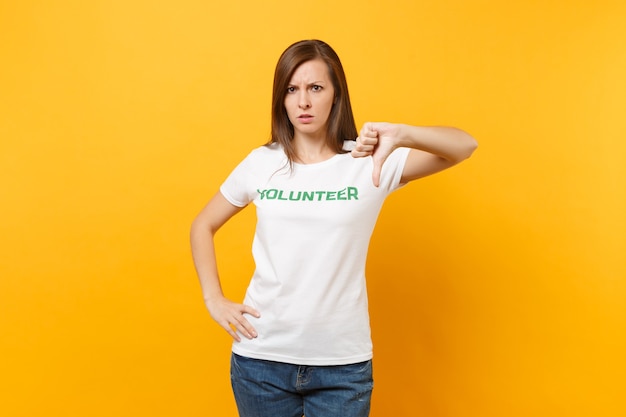 Portrait of sad upset shocked young woman in white t-shirt with written inscription green title volunteer isolated on yellow background. Voluntary free assistance help, charity grace work concept.