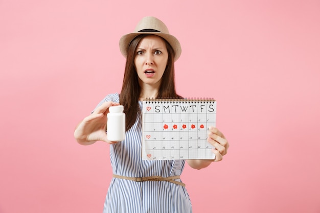 Portrait of sad woman in blue dress holding white bottle with pills, female periods calendar, checking menstruation days isolated on background. Medical healthcare, gynecological concept. Copy space.