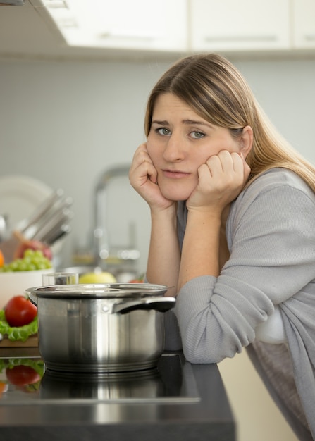 Ritratto di donna triste appoggiata al tavolo in cucina mentre cucina