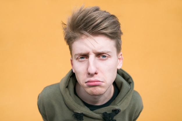 Portrait of a sad young man on an orange wall. funny guy on a bright wall close up