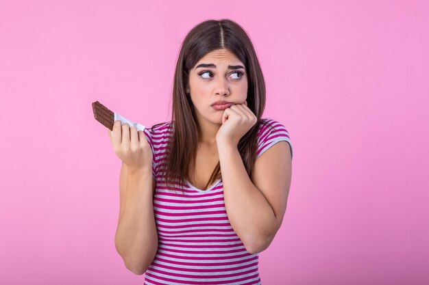 Photo portrait sad young woman tired of diet restrictions craving sweets chocolate isolated on pink wall background human face expression emotion nutrition concept feeling of guilt passion for chocolate