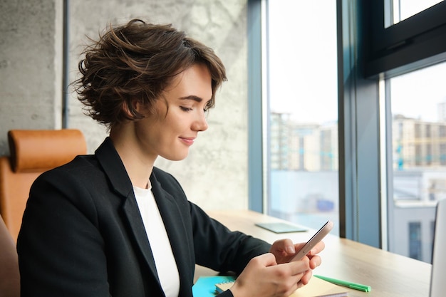 Photo portrait of saleswoman answering message reading smartphone sitting in an office