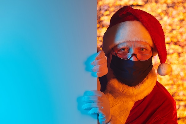Portrait of Santa Claus in hat and in protective mask  standing behind the wall