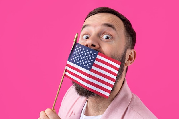 Portrait of a satisfied young man with a beard with an American flag on a red studio background Great US patriot and defender of freedom