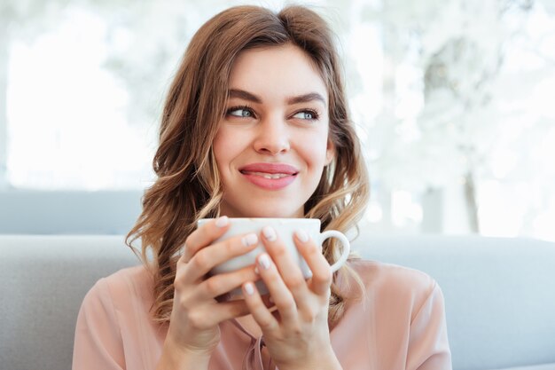 一杯のコーヒーを保持している満足している若い女性の肖像画