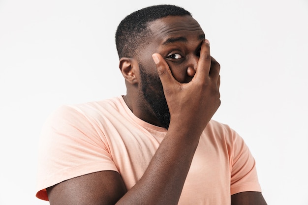 Portrait of a scared african man wearing t-shirt standing isolated over white wall, cover mouth