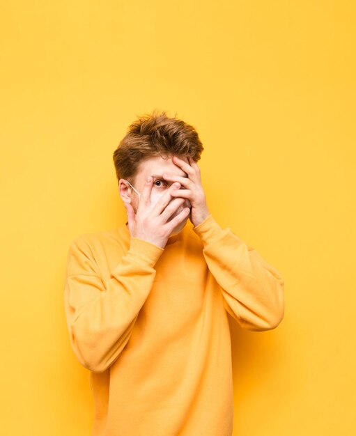 Portrait of a scared guy in a yellow sweatshirt and a protective medical mask