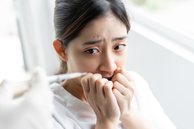 Portrait of a scared young girl in front of a syringe