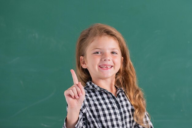 Portrait of school girl nerd pupil with surprising expression pointing with finger against blackboard