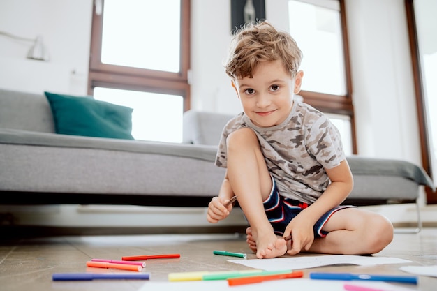 家の居間の木の床に座っている学齢期の少年の肖像画少年