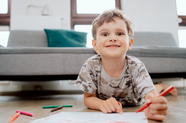 家の居間の木の床に座っている学齢期の少年の肖像画少年