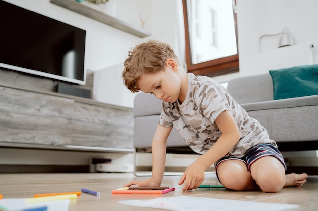 家の居間の木の床に座っている学齢期の少年の肖像画少年