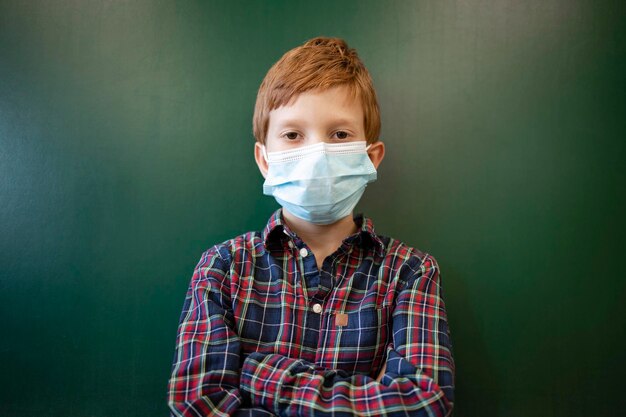 Photo portrait of schoolboy wearing protective face mask and standing by the board in classroom