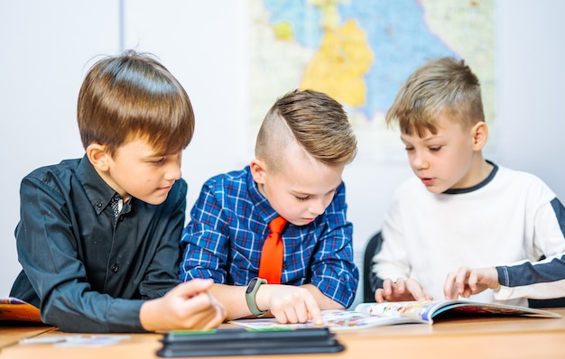 Portrait of schoolboys looking at textbooks together with other pupils during a lesson in modern smart school. Selective focus. Side view