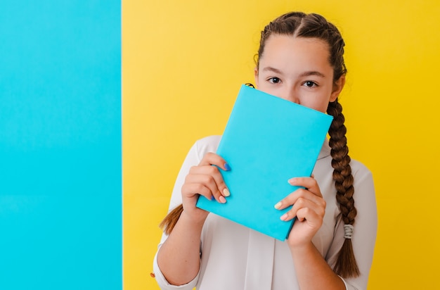 Portrait of a schoolgirl in glasses with books textbooks on yellow blue 