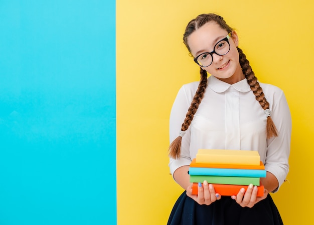 Portrait of a schoolgirl in glasses with books textbooks on yellow blue 