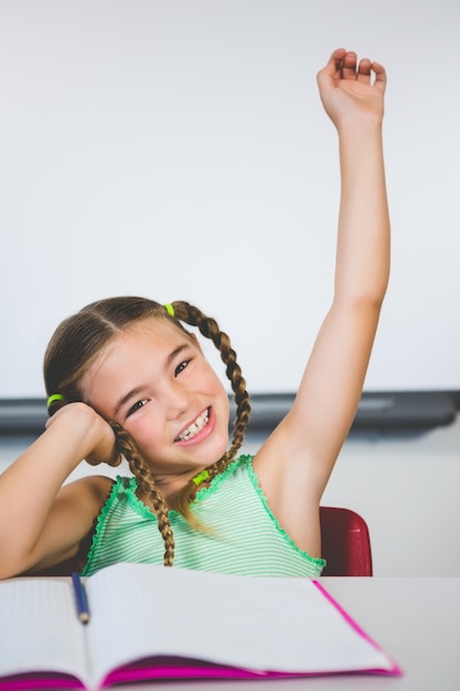 Portrait of schoolgirl raising her hand in classroom