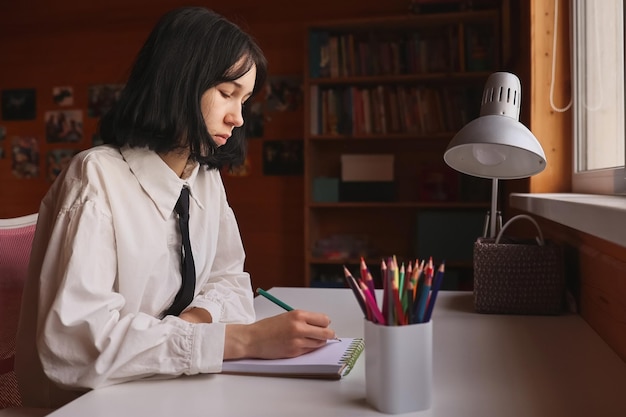 Portrait of the schoolgirl siting at the table indoors and doing her homework The girl does homework at home Distance learning Lessons homework education