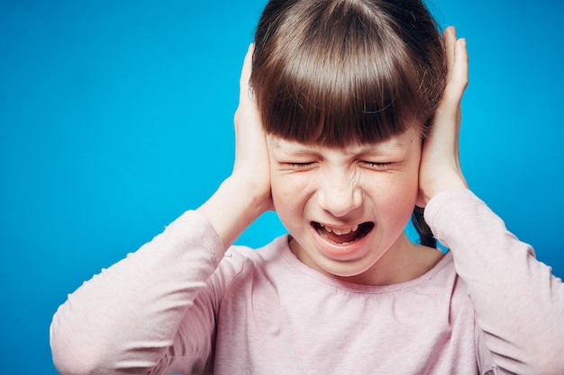 Portrait of a screaming girl with tightly shut eyes. child covering ears with hands