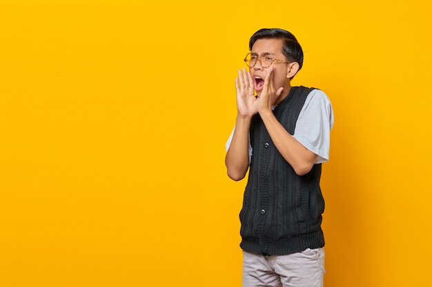 Portrait of screaming young Asian man with shocked expression on yellow background