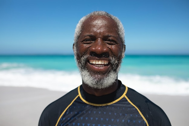 Portrait of a senior African American man on a beach in the sun, looking to camera and smiling, with blue sky and sea in the background